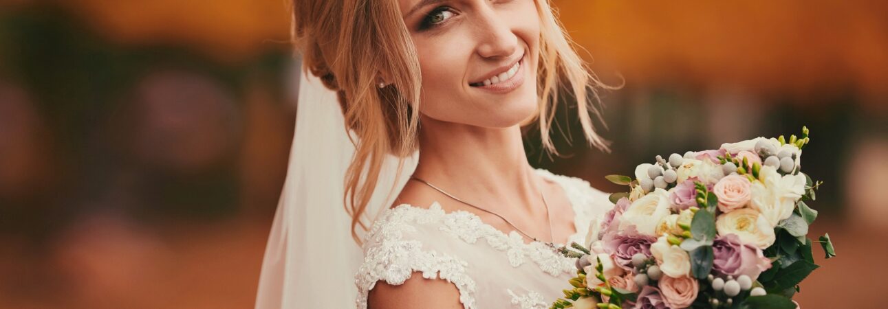 Beautiful bride smelling wedding bouquet in autumn park close up on wedding day