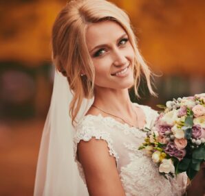 Beautiful bride smelling wedding bouquet in autumn park close up on wedding day