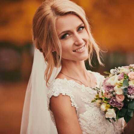 Beautiful bride smelling wedding bouquet in autumn park close up on wedding day